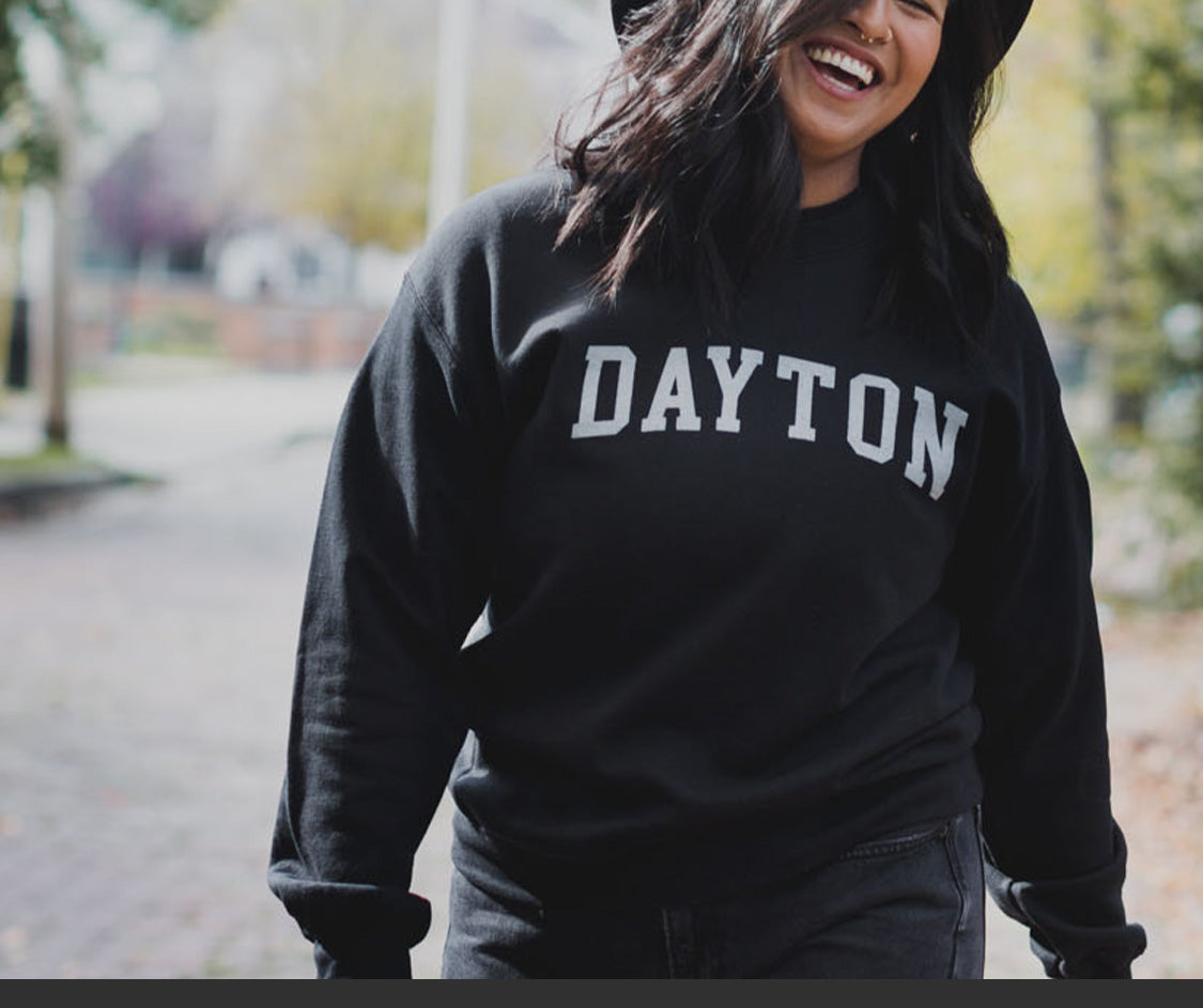 Person wearing a black sweatshirt with 'DAYTON' printed on it, standing outdoors.